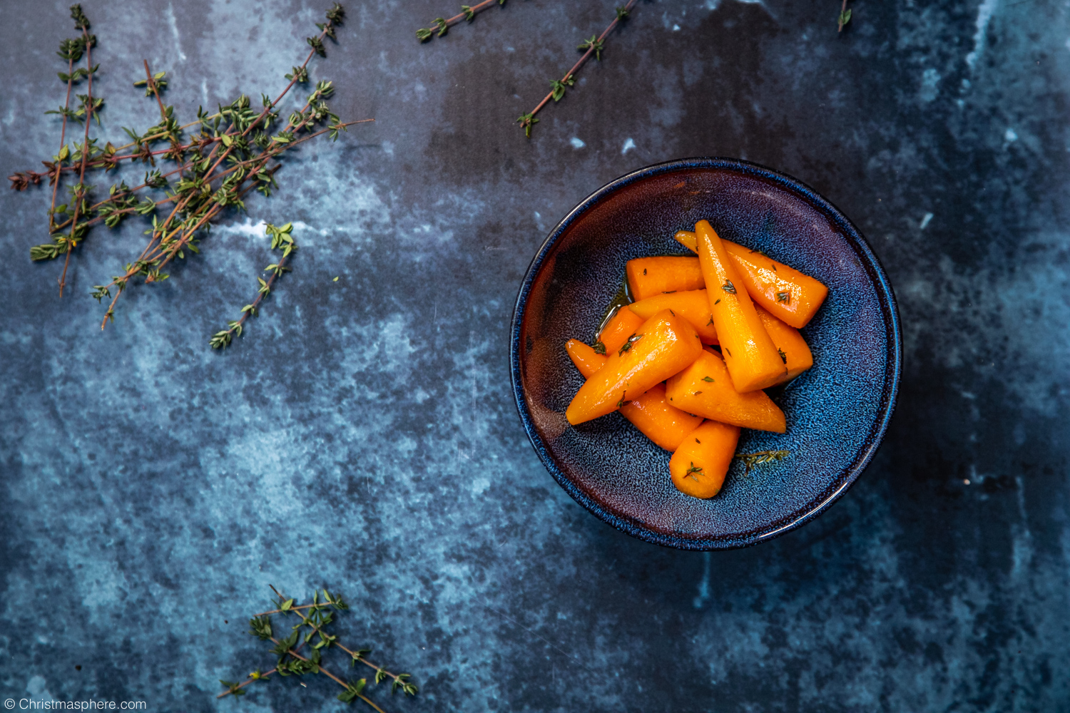 Glazed carrots with fresh thyme in blue bowl and thyme sprigs scattered around