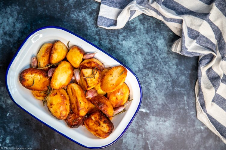 Bowl of crispy roast potatoes with a blue and white tea towel in the corner