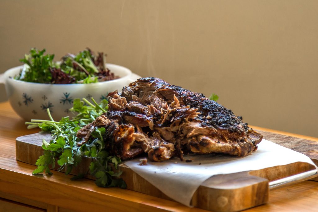 Slow Roasted Lamb Shoulder on a wooden chopping board. There is a bowl of fresh green salad in the background.
