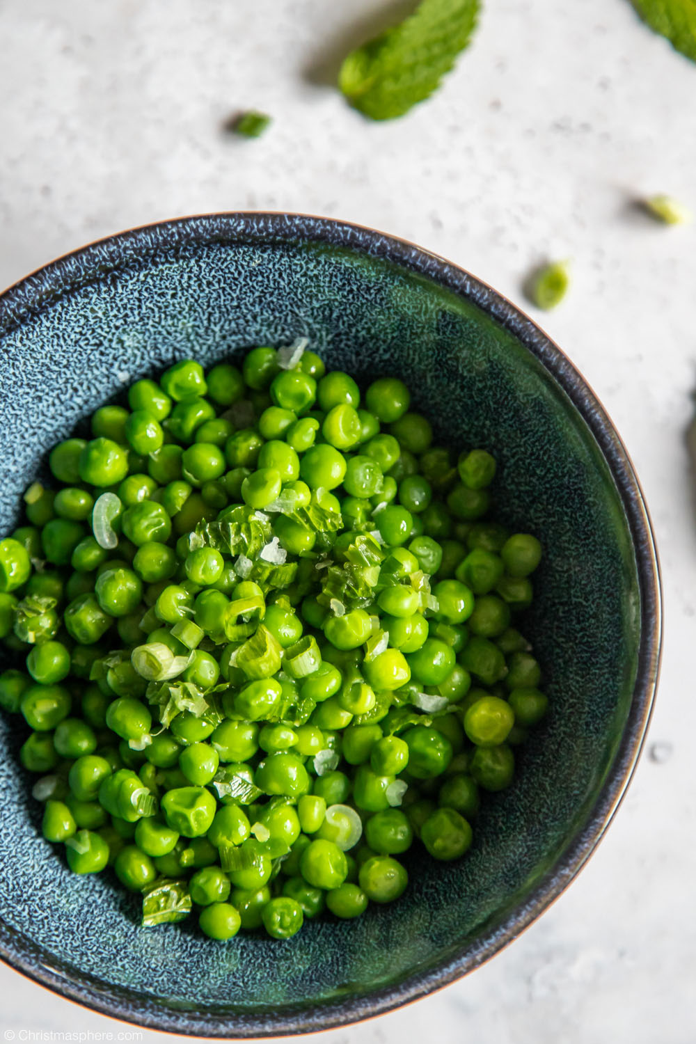 Birds eye view of a blue bowl containing peas with mint and spring onion