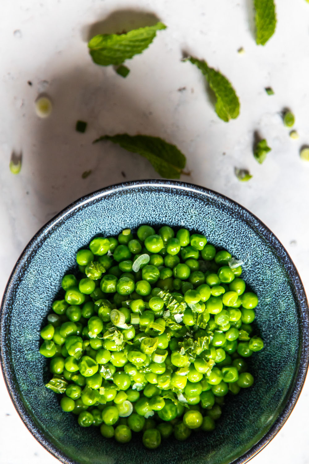 Top view of bowl of peas surrounded by mint and spring onions