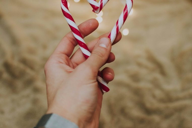hand holding candy canes in a heart shape with fairy lights in the background