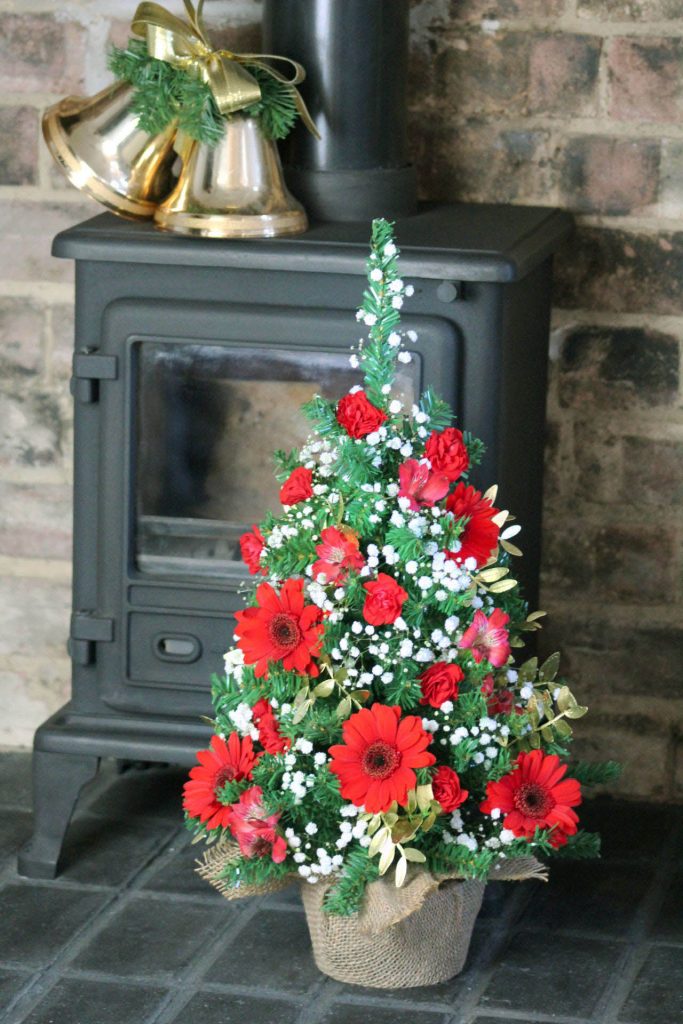 Small Christmas tree with flowers by fireplace