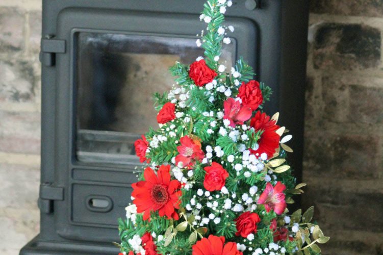 Small Christmas tree with flowers by fireplace