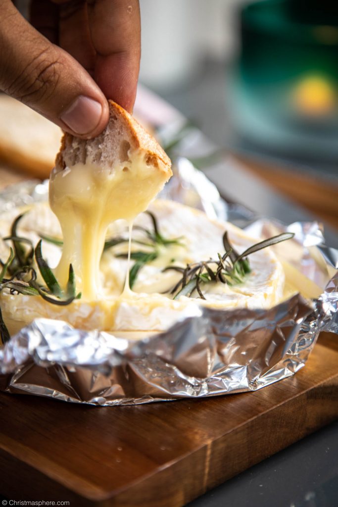 Hand dipping bread into melted camembert cheese
