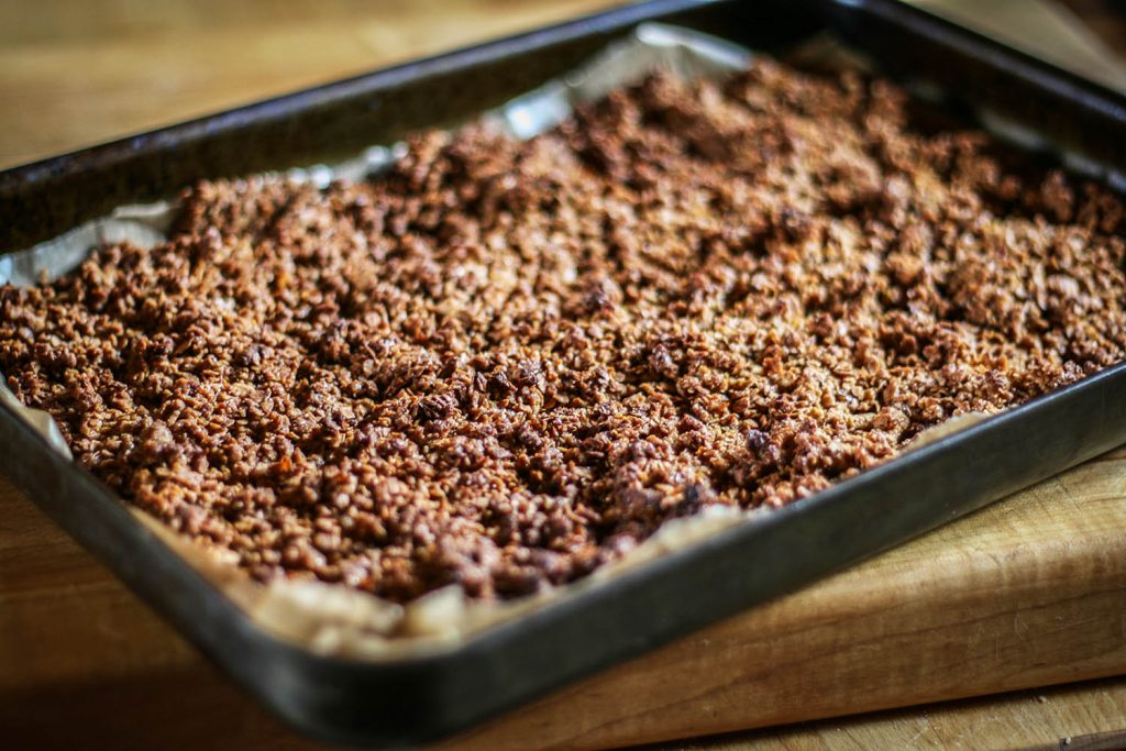 Baking tray lined with baking paper on top is layer of baked granola