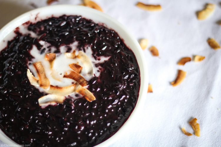 Top view of bowl of black rice pudding with a drizzle of coconut cream and toasted coconut flakes