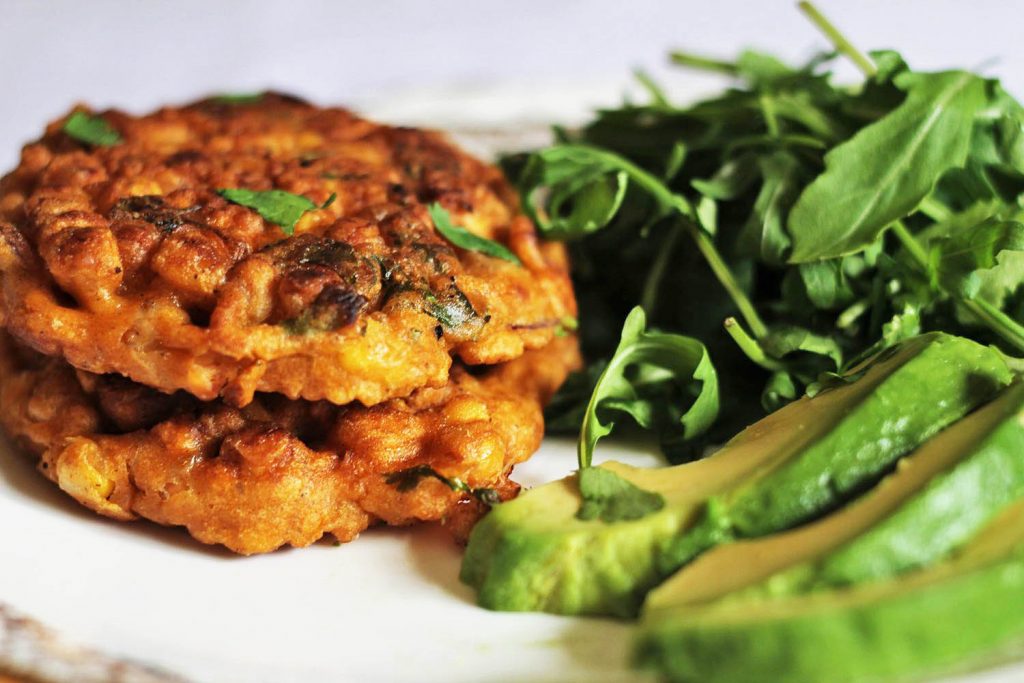Close up of two sweetcorn fritters on a plate with rocket and avocado sides