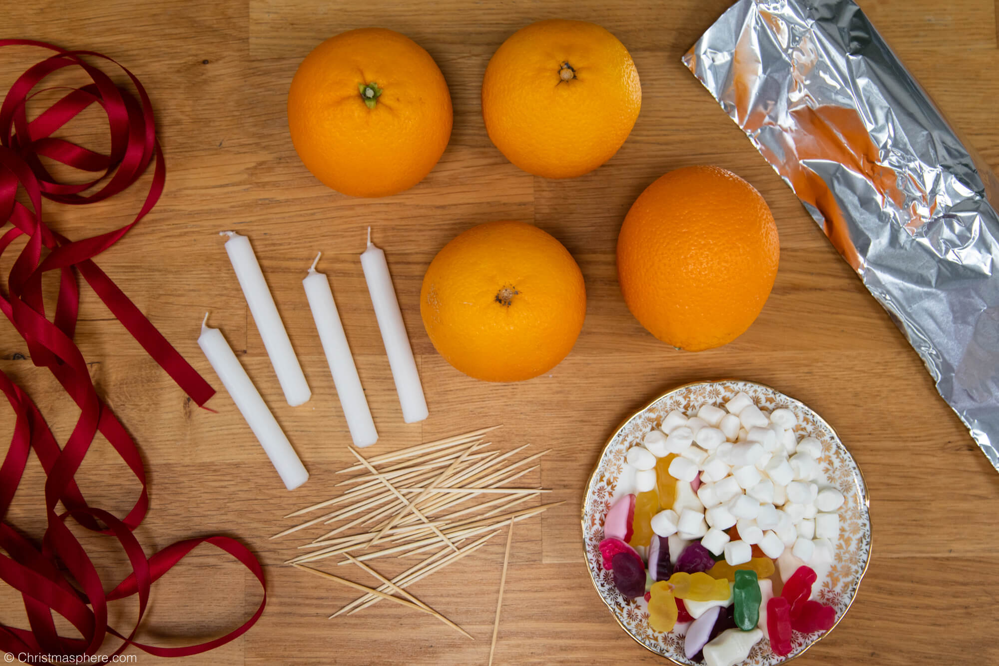 red ribbon, white candles, oranges, plate of sweets, tin foil, cocktail sticks