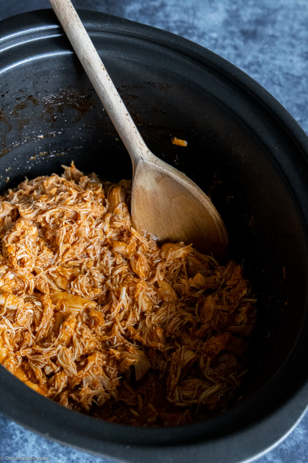Shredded Chicken in a slow cooker pot with a wooden spoon